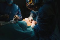 Von unten näht plastischer Chirurg die Brust einer Patientin nach dem Einsetzen von Implantaten im Operationssaal zu — Stockfoto