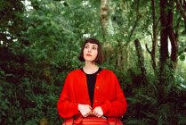 Donna in rosso con valigia rossa passeggiando nel verde della foresta — Foto stock