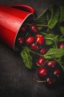 Tasty appetizing ripe cherries with leaves falling from red cup on black surface — Stock Photo