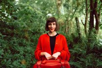 Frau in Rot mit großem roten Koffer spaziert im grünen Wald — Stockfoto