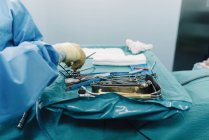De cima médico de colheita em uniforme colocando tesoura na bandeja com ferramentas cirúrgicas inoxidáveis na sala de cirurgia — Fotografia de Stock