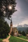 Pequena igreja na colina verde sob sol brilhante e montanhas rochosas no fundo em Dolomites, Itália — Fotografia de Stock