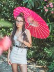 Jovem mulher pensativa em roupa de verão com guarda-chuva em pé no parque — Fotografia de Stock