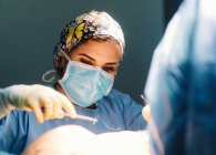 Plastic surgeon sewing up breast of female patient after inserting implants in operating room — Stock Photo