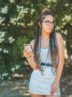 Стильна молода жінка в окулярах і літній одяг з використанням смартфона і дивлячись у парк — стокове фото