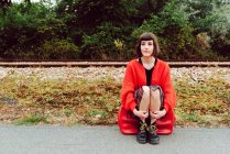 Nachdenkliche Frau sitzt auf rotem Koffer auf Straße in Bahnnähe — Stockfoto