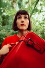 Donna in rosso con grande valigia rossa passeggiando nella foresta verde — Foto stock