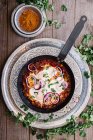 From above tasty aromatic shakshuka decorated with onion and greens on pan on silver plate and turmeric in bowl on wooden table — Stock Photo