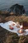 Коврик для пикника с романтическим набором с бокалами напитков и едой на сухом берегу с безмятежной водой — стоковое фото