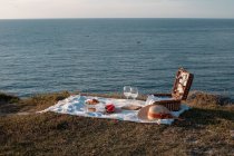 Esterilla de picnic con romántico conjunto con vasos de bebida y comida en la orilla seca con agua serena - foto de stock