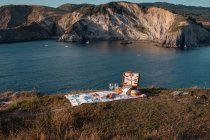Esterilla de picnic con romántico conjunto con vasos de bebida y comida en la costa rocosa del mar - foto de stock