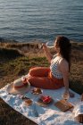Young woman romantically drinking wine on shore near serene water and hills — Stock Photo