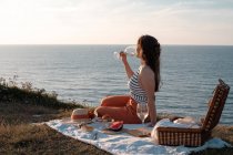 Junge Frau trinkt romantisch Wein am Ufer in der Nähe von heiterem Wasser und Hügeln — Stockfoto