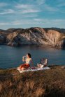 Jeune femme buvant romantiquement du vin sur la côte près de l'eau sereine et des collines — Photo de stock