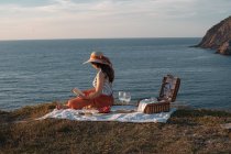 Vista lateral de la mujer en sombrero con libro sentado en la estera para picnic con sandía - foto de stock