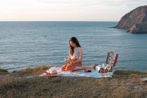 Vista laterale della donna con libro seduto su tappetino per picnic con anguria sulla riva asciutta — Foto stock