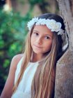 Портрет маленькой красивой девушки в белом платье цветок ободок опираясь на стену и глядя в камеру — стоковое фото