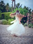 Симпатична маленька дівчинка в білій повітряній сукні та квітковій смузі, що обертається в парку — стокове фото