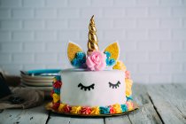 Cute unicorn cake with painted closed eyes on wooden table — Stock Photo