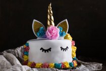 Cute unicorn cake with painted closed eyes on cloth on black background — Stock Photo