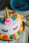 Bonito pastel de unicornio con ojos cerrados pintados en la mesa de madera - foto de stock