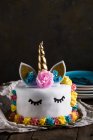 Carino unicorno torta con occhi chiusi dipinti su tavolo di legno su sfondo scuro — Foto stock