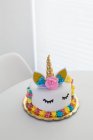 Bonito pastel de unicornio con los ojos cerrados pintados en la mesa blanca - foto de stock