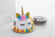 Bonito pastel de unicornio con los ojos cerrados pintados en la mesa blanca - foto de stock