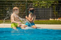 Espalhando crianças felizes na borda da piscina se divertindo e jogando juntos em dia ensolarado brilhante — Fotografia de Stock