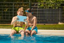 Boys on poolside browsing tablet — Stock Photo