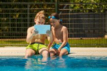 Boys on poolside browsing tablet — Stock Photo