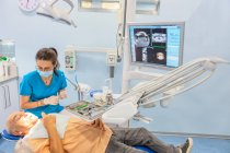 Стоматолог одягає хірургічні рукавички, коли пацієнт лежить у кріслі — стокове фото