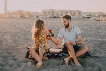 Amorous homme donnant charmante femme rose sur la plage au coucher du soleil soir — Photo de stock