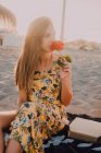 Charming thoughtful woman with rose in hand sitting and looking away alone in sunlight on seaside — Stock Photo