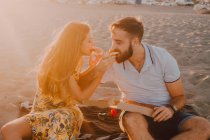 Bearded amorous man and long-haired woman feeding each other with tenderness in sunlight — Stock Photo