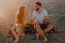 Homme amoureux barbu et femme aux cheveux longs se nourrissant mutuellement avec tendresse au soleil — Photo de stock