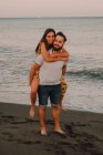 Bearded man giving woman piggyback ride in foamy water seaside — Stock Photo