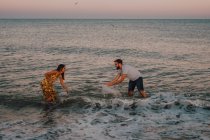 Verliebte junge Leute planschen und spielen im Wasser unter heiterem Himmel mit Möwe — Stockfoto