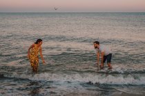 Jovens amorosos salpicando e brincando na água sob céu sereno com gaivota — Fotografia de Stock