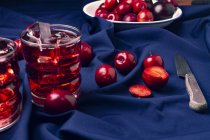 Bebida vermelha perto de frutas frescas em pano azul — Fotografia de Stock