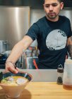 Hombre joven en camiseta negra que pone en el tazón de la tabla del plato japonés cocinado fresco llamado ramen - foto de stock