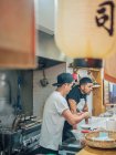 Vista laterale di multirazziale giovani uomini cucina piatto giapponese chiamato ramen in ristorante asiatico e guardando in macchina fotografica — Foto stock