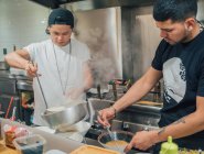Les jeunes hommes versant le bouillon chaud de la casserole pour plat japonais appelé ramen dans le café asiatique — Photo de stock