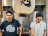 Молоді мультирасової чоловіки, що готують і обслуговують японські страви рамен в азіатському бістро — стокове фото