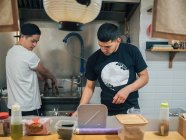 Young multiracial men cooking and serving Japanese dish ramen in Asian bistro — Stock Photo