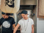 Chefs masculinos multiétnicos cocinando comida asiática en la cafetería - foto de stock