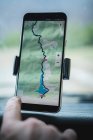 Closeup hand of anonymous tourist using GPS navigator on modern smartphone in car during road trip — Stock Photo