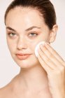 Freckled woman cleansing face skin face with lotion on cotton sponge isolated on white background — Stock Photo