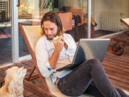 Man with laptop and apple core with asking spaniel dog on balcony — Stock Photo