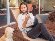 Homme avec ordinateur portable et noyau de pomme avec chien d'épagneul demandant sur le balcon — Photo de stock